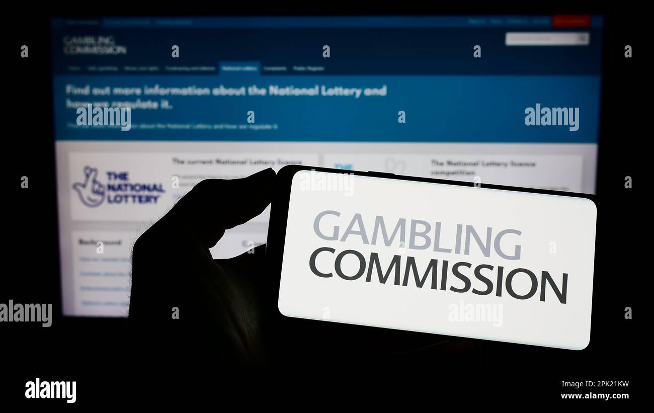 Person, die ein Handy mit dem Logo der britischen öffentlichen Körperschaft Gambling Commission auf dem Bildschirm vor der Webseite hält. Konzentrieren Sie sich auf das Display des Telefons. Stockfoto