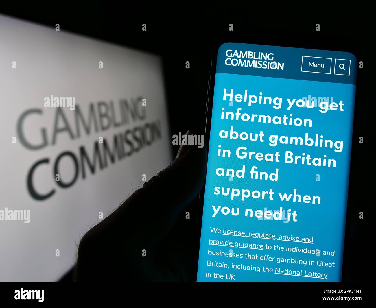 Person, die ein Handy mit einer Website der britischen öffentlichen Körperschaft Gambling Commission auf dem Bildschirm vor dem Logo hält. Konzentrieren Sie sich auf die Mitte des Telefondisplays. Stockfoto