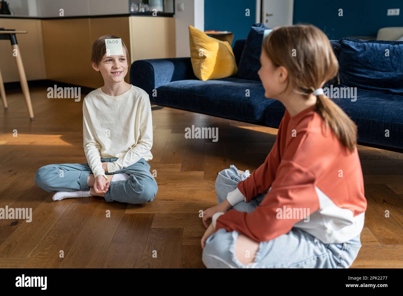 Lächelnde Teenager-Schwester und kleiner Bruder spielen "Who am i" Spiel sitzen auf dem Boden zu Hause im Wohnzimmer. Stockfoto