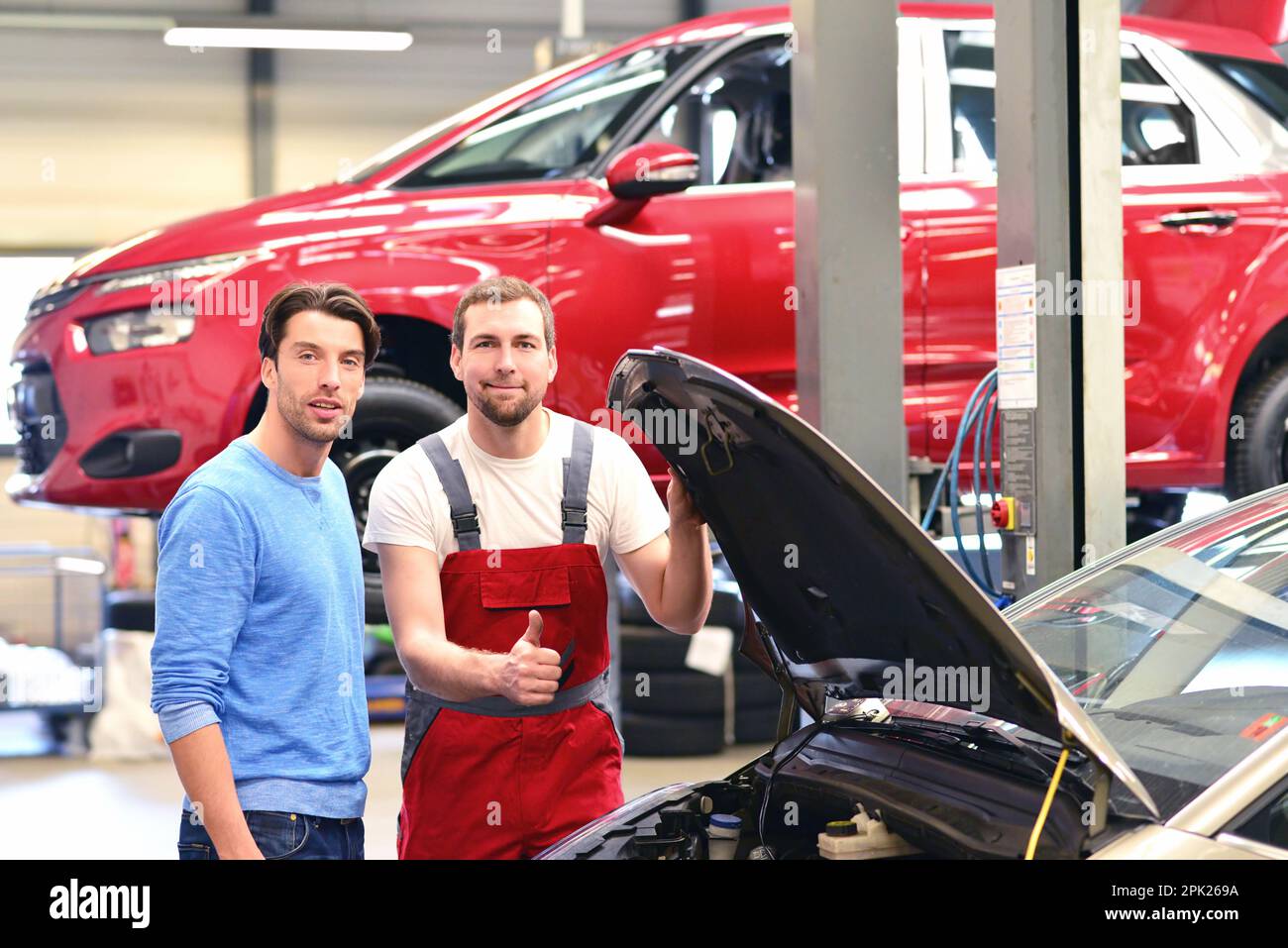 After-sales-Service in der Autowerkstatt - Mechaniker und Mann sprechen über die Reparatur eines Fahrzeugs Stockfoto