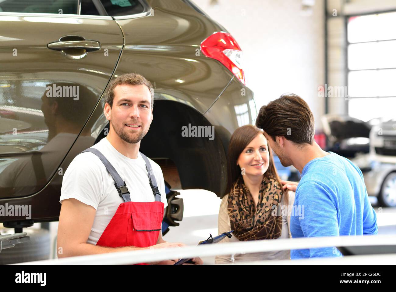 Kundendienst in der Garage – Mechaniker und junge Paare sprechen über die Reparatur eines Fahrzeugs Stockfoto