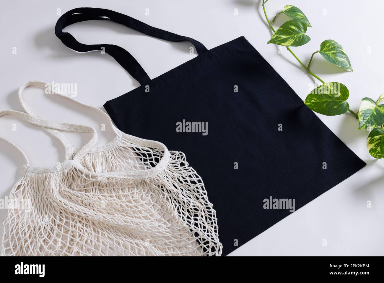 Großer Blickwinkel auf weiße Netz- und schwarze Leinentasche mit Kopierbereich und Pflanze auf weißem Hintergrund Stockfoto