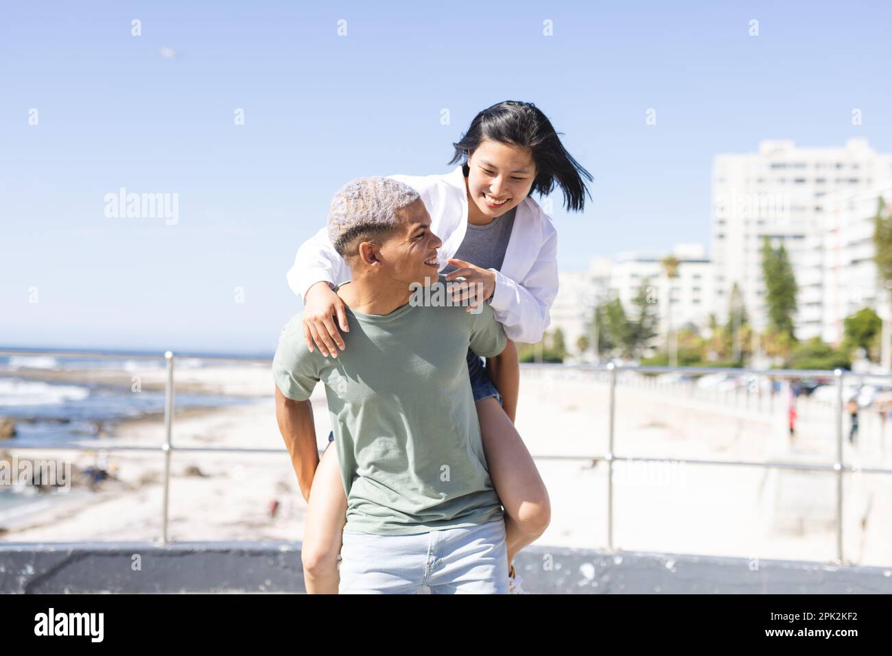 Glückliches, vielfältiges Paar, das Zeit miteinander verbringt und sich auf der Promenade am Meer umgibt Stockfoto