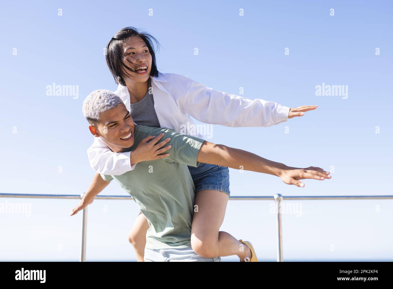 Glückliches, vielfältiges Paar, das Zeit miteinander verbringt und sich auf der Promenade am Meer umgibt Stockfoto