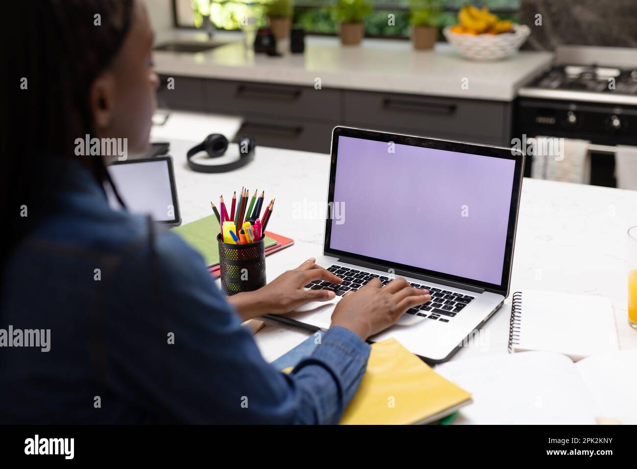 Eine afroamerikanische Teenagerin, die Hausaufgaben macht, einen Laptop mit Kopierraum benutzt Stockfoto