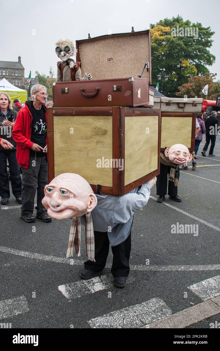 Puppenspieler und Puppenspieler mit dem Rücken brechenden Tragen von Teekiste und Koffern, gesehen beim Skipton International Puppet Festival, North Yorkshire, Großbritannien Stockfoto