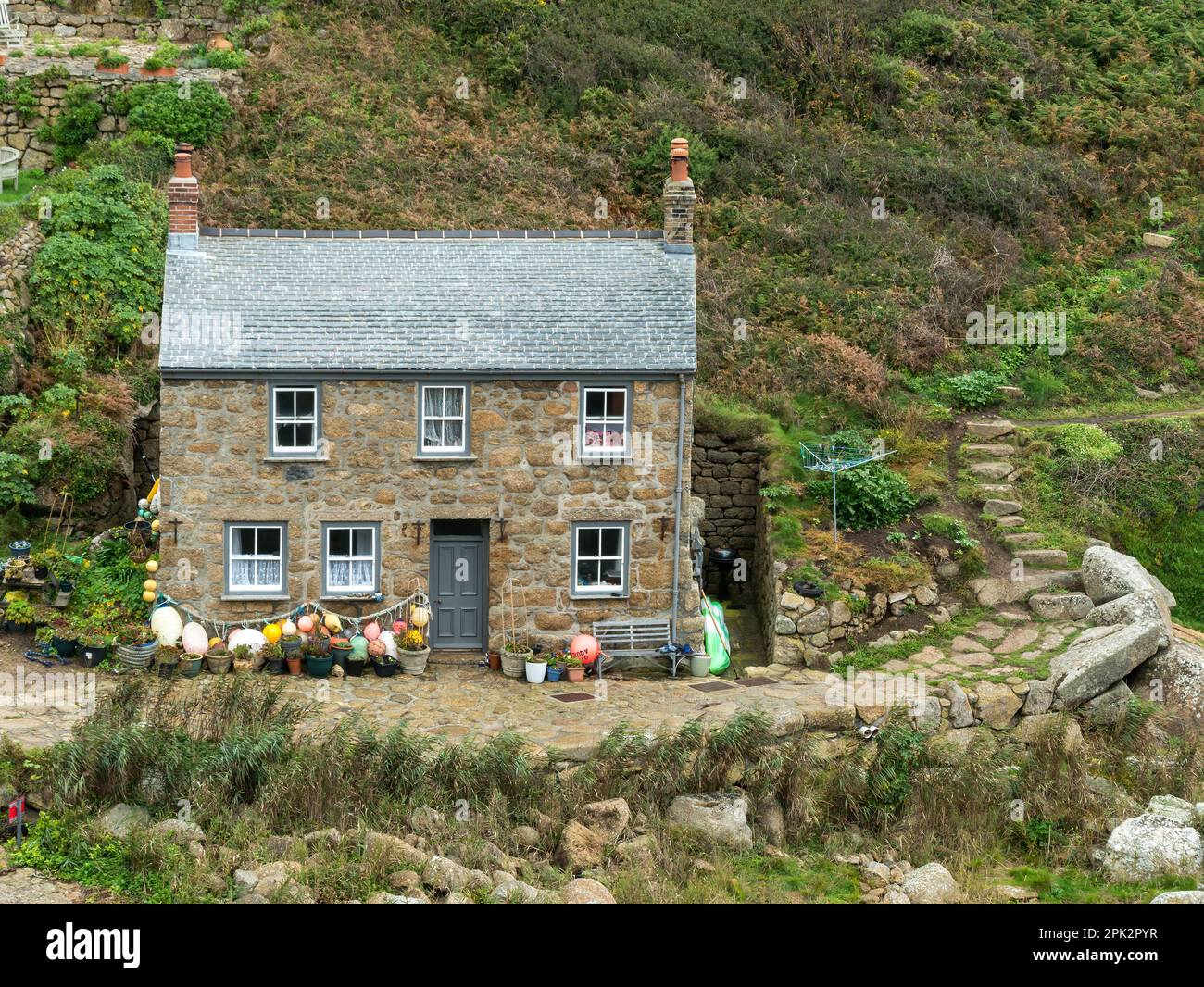 Attraktive alte Granitsteinhütte am Meer in Cornish mit Schieferdach und Fischerboote und Bojen in Penberth Cove, Cornwall, Großbritannien Stockfoto