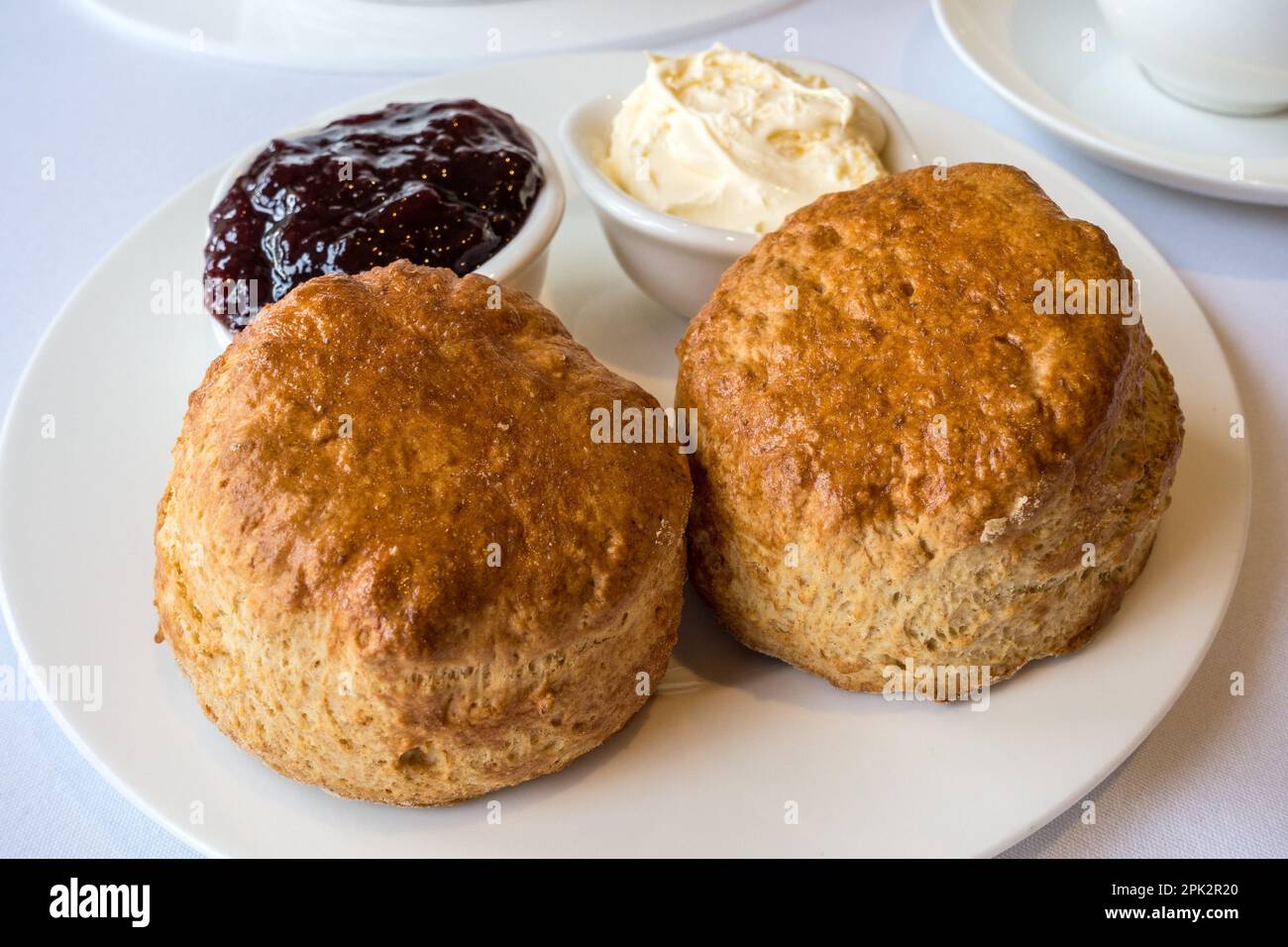 Cream Tea mit zwei frisch gebackenen einfachen Scones mit kleinen Gerichten aus Clotted Cream und Erdbeermarmelade auf einem sauberen weißen Teller und Tischdecke, England, Großbritannien Stockfoto