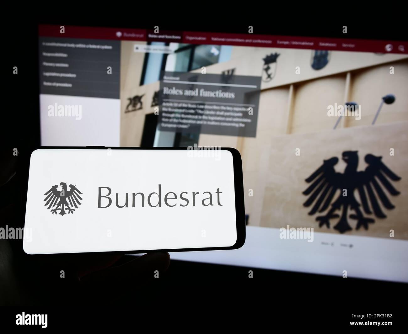 Person, die ein Mobiltelefon mit dem Siegel des deutschen Bundesrats auf dem Bildschirm vor der Webseite hält. Konzentrieren Sie sich auf das Display des Telefons. Stockfoto