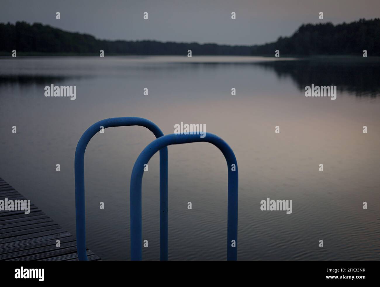 Ein atemberaubender Blick in der Abenddämmerung auf ein hölzernes Dock, das in ein ruhiges Gewässer hinausschaut, eingebettet in eine ruhige ländliche Landschaft Stockfoto