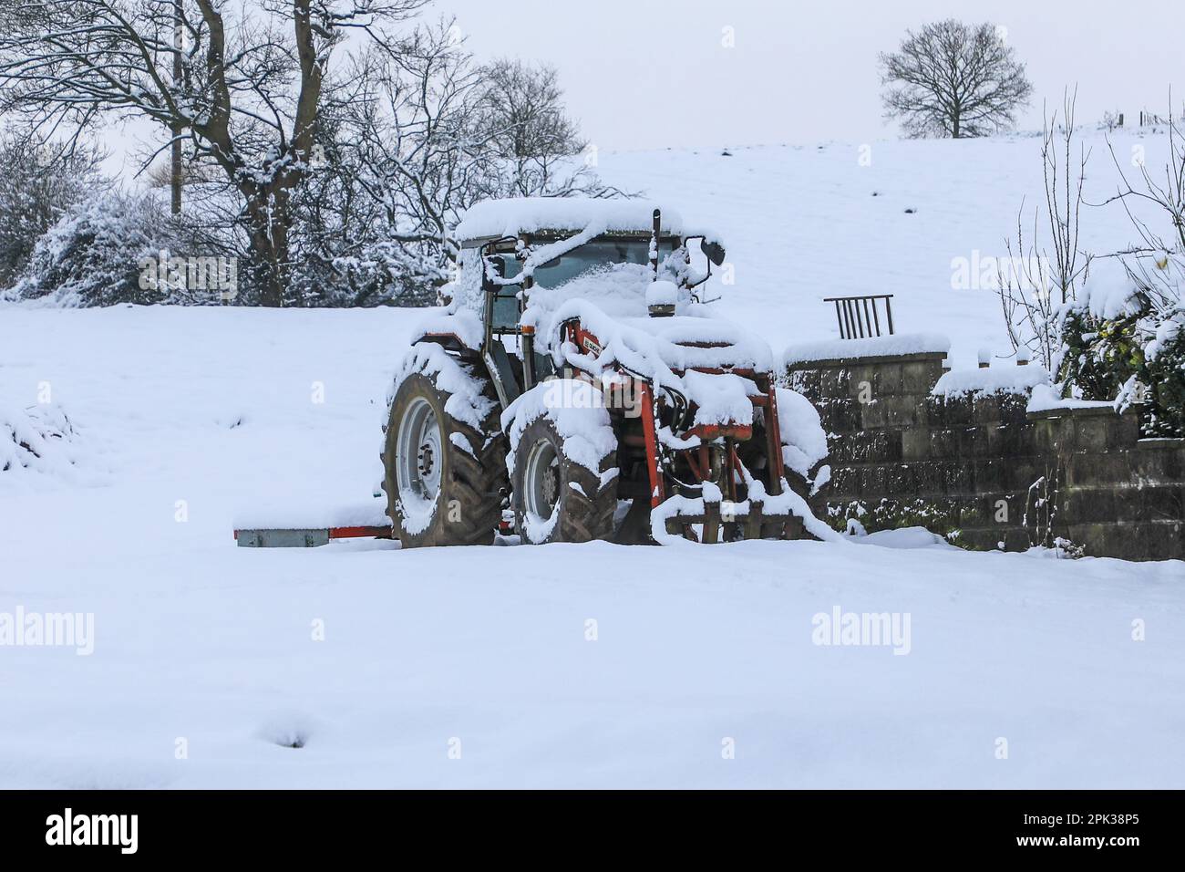 Ein Traktor, der an einem verschneiten Wintertag in England mit Schnee bedeckt ist Stockfoto
