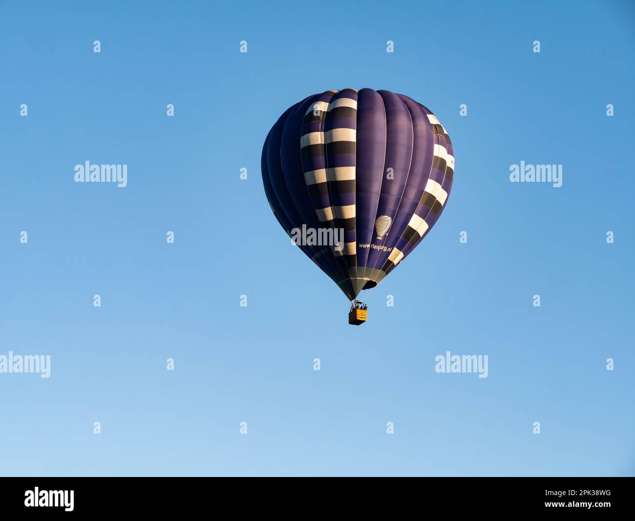 Dunkelblauer Heißluftballon mit Menschen im Korb, die in der Luft fliegen und wolkenloser blauer Himmel, Niederlande Stockfoto