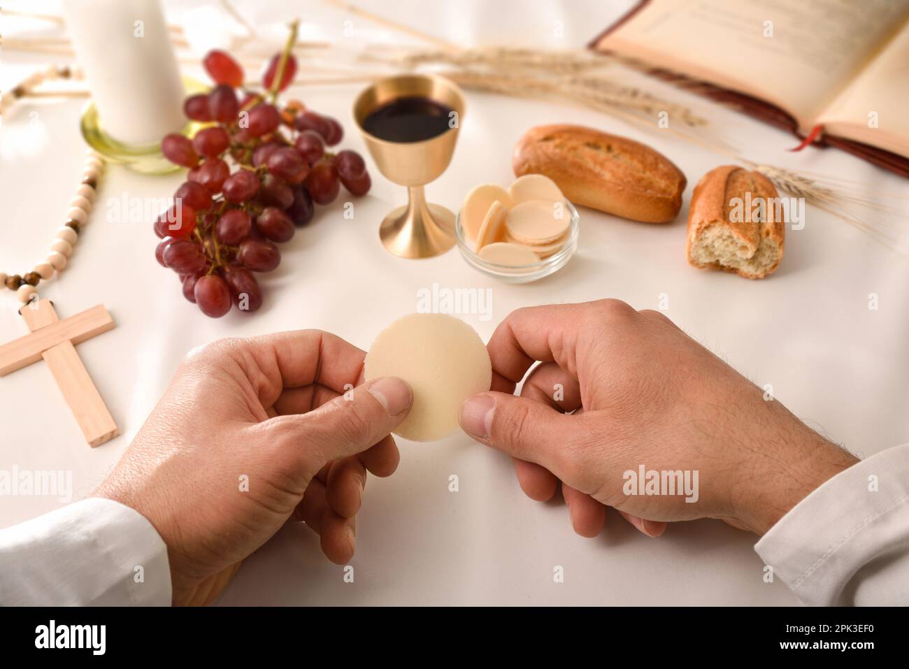 Der Priester des Eucharisten weiht das Brot, um es an die Kommunikanten zu verteilen, auf einem Tisch am Altar mit Ausrüstung für das Sakrament. Erhöht Stockfoto