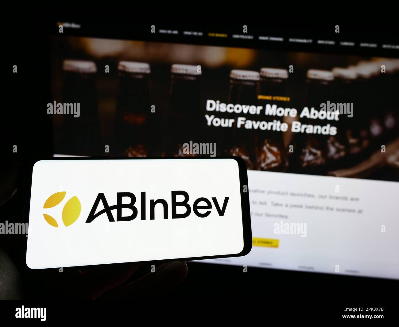 Person, die ein Mobiltelefon mit dem Logo des Brauereiunternehmens Anheuser-Busch InBev (ab InBev) auf dem Bildschirm vor der Webseite hält. Konzentrieren Sie sich auf das Display des Telefons. Stockfoto