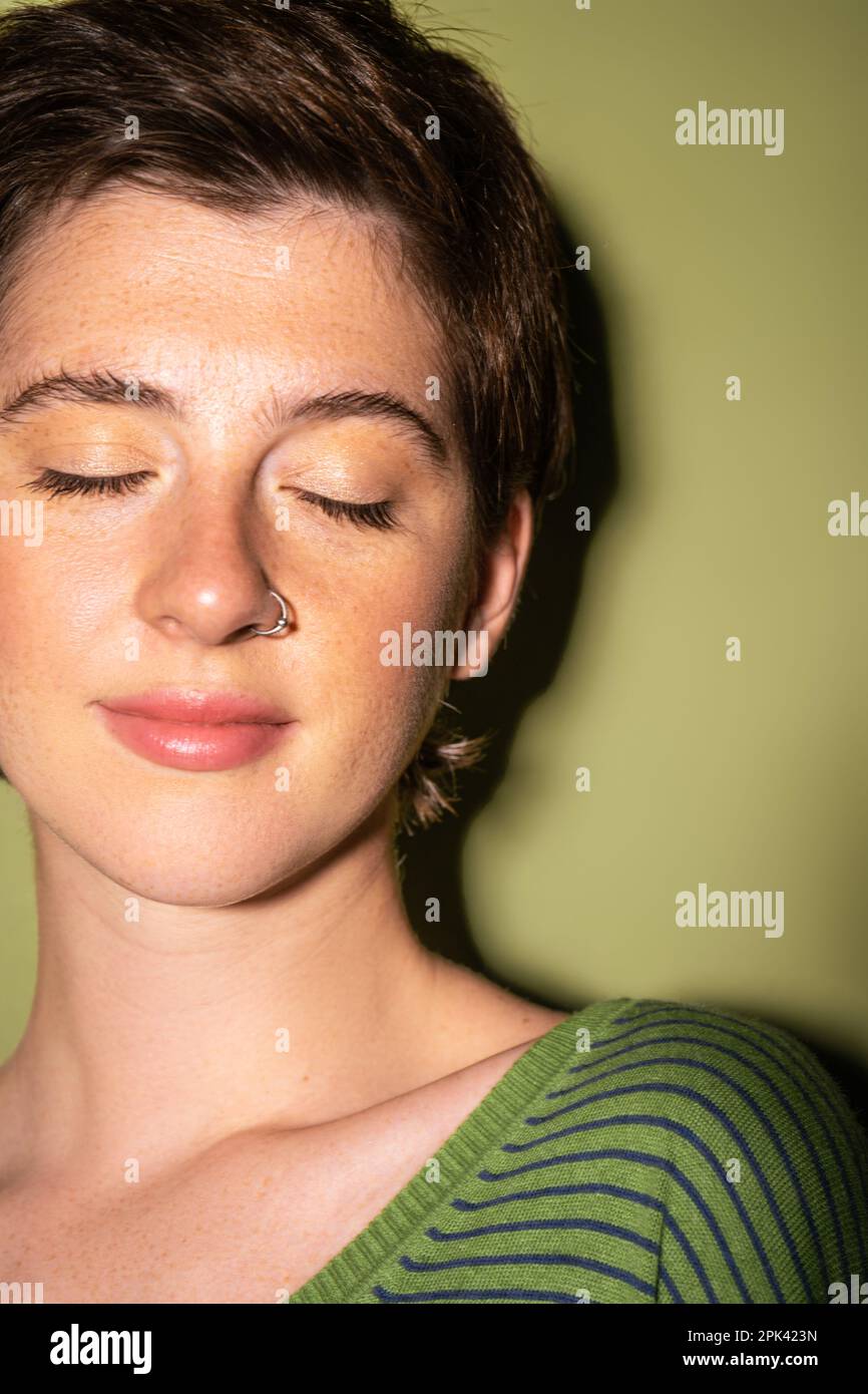 Porträt einer traumhaften Frau mit Sommersprossen und lächelnder Nase mit geschlossenen Augen auf grünem Hintergrund, Stockbild Stockfoto