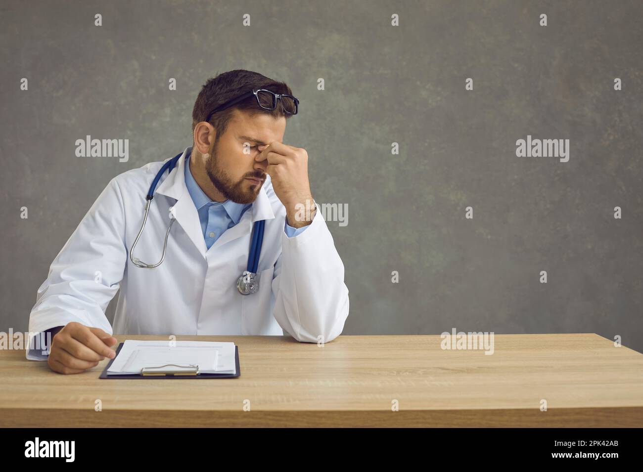 Müde, erschöpfter männlicher Arzt, der nach einem harten Arbeitstag am Tisch sitzt. Medizinischer Alltag. Stockfoto