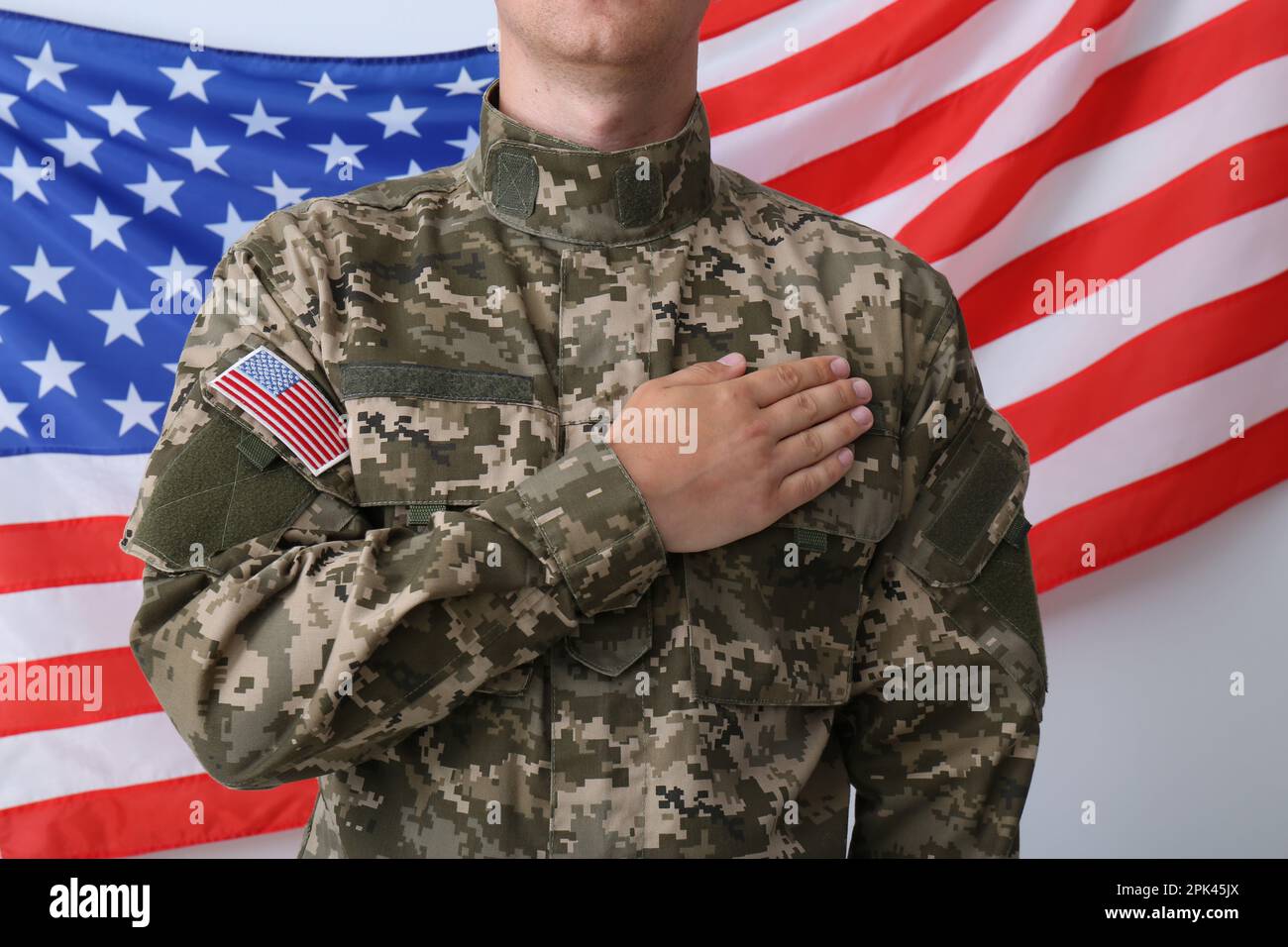 Ein Soldat, der Hand am Herzen hält, nahe der Flagge der Vereinigten Staaten von Amerika auf weißem Hintergrund, Nahaufnahme Stockfoto