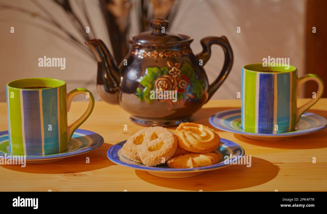 Tassen Tee mit einem Teller Kekse und einer Teekanne im Hintergrund. Stockfoto