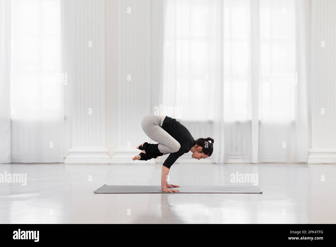 Seitenansicht einer charmanten Frau, die bakasana während der Yoga-Meditation in einem hellen Fitnessstudio macht. Das Konzept der Armfestigkeit und -Ausdauer, -Flexibilität und -Balance Stockfoto