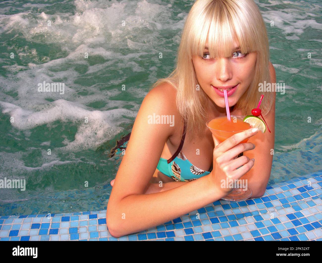 Junge, wunderschöne Frau, die sich mit einem Cocktail im Swimmingpool entspannen kann Stockfoto