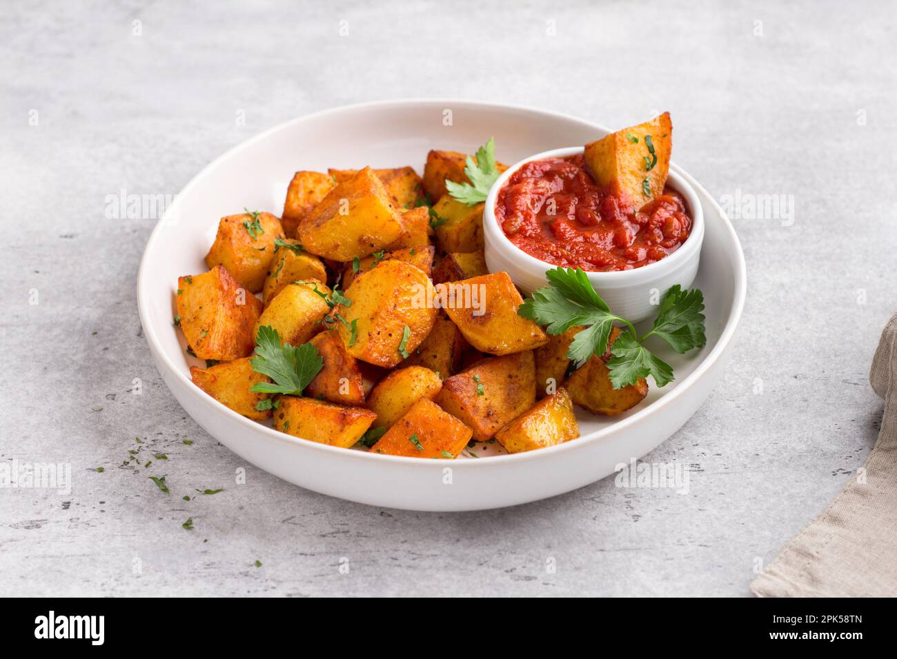 Traditionelle spanische Kartoffel, Patatas bravas mit geräucherter Paprika, scharfe Tomatensoße und Petersilie in einer weißen Schüssel auf grauem Steinhintergrund, Draufsicht. D Stockfoto