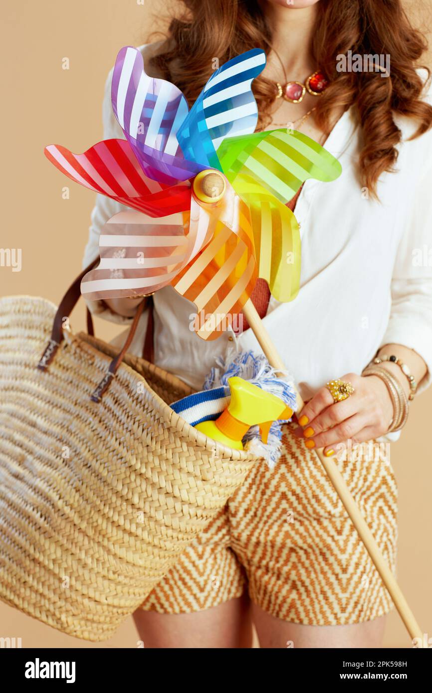 Strandurlaub. Nahaufnahme einer Frau in weißer Bluse und Shorts, isoliert auf Beige mit Windmühlen-Spielzeug. Stockfoto Strandurlaub. Nahaufnahme einer Frau in weißer Bluse und Shorts, isoliert auf Beige mit Windmühlen-Spielzeug. Stockfoto