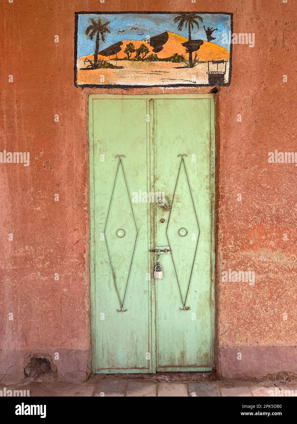 Sahara-Wüste, Marokko, Afrika: Grüne eiserne Tür und Zeichen von Wüste und Palmen in Merzouga, Abfahrtsort für Touristen, die die Dünen von Erg Chebbi besuchen Stockfoto