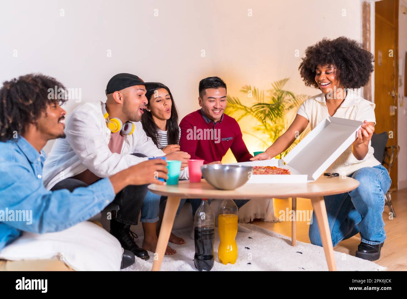 Eine Gruppe multiethnischer Freunde auf dem Sofa isst Pizza und trinkt