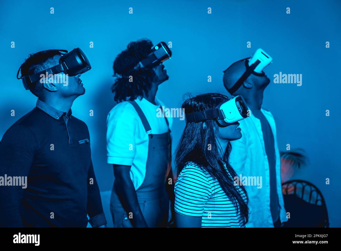 Gruppe junger Menschen mit VR-Brille in einem Virtual-Reality-Spiel im blauen Licht, futuristisch oder wissenschaftlich, technologisches Konzept, mit Blick nach rechts Stockfoto