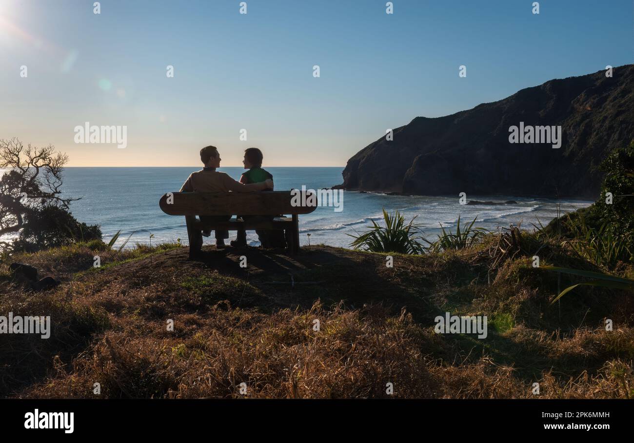 Ein Paar, das sich ansieht, auf der Bank am Bethells Beach sitzt. Ein Paar in der Liebe Konzept. Waitakere. Auckland. Stockfoto