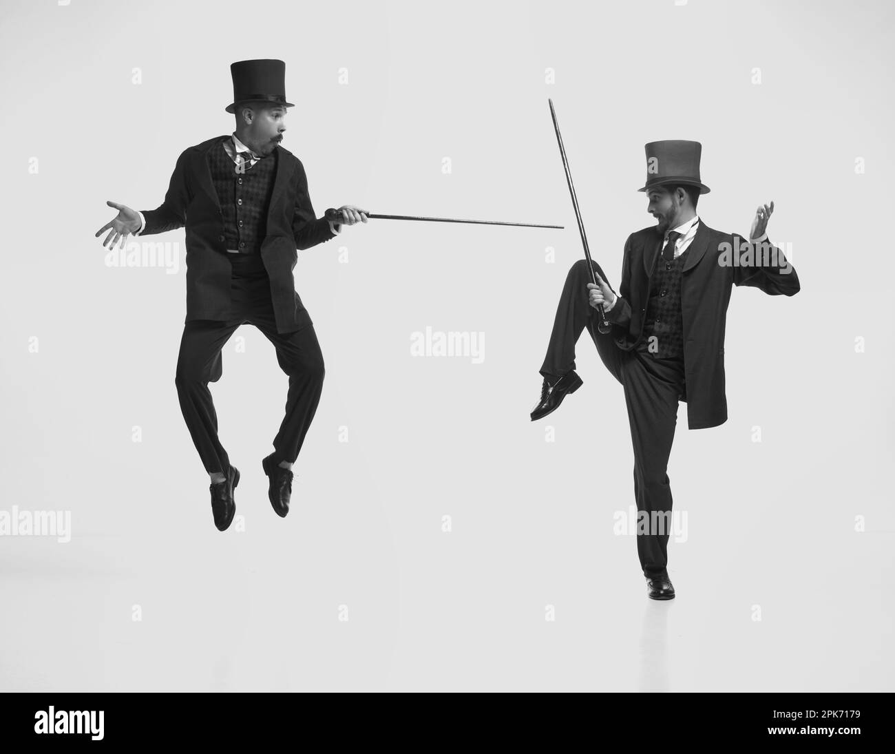 Schwarz-weißes Porträt von zwei Herren, die klassische Anzüge tragen, springen und kämpfen mit Stöcken. An die Kindheit erinnert. Schwarzweiß Stockfoto