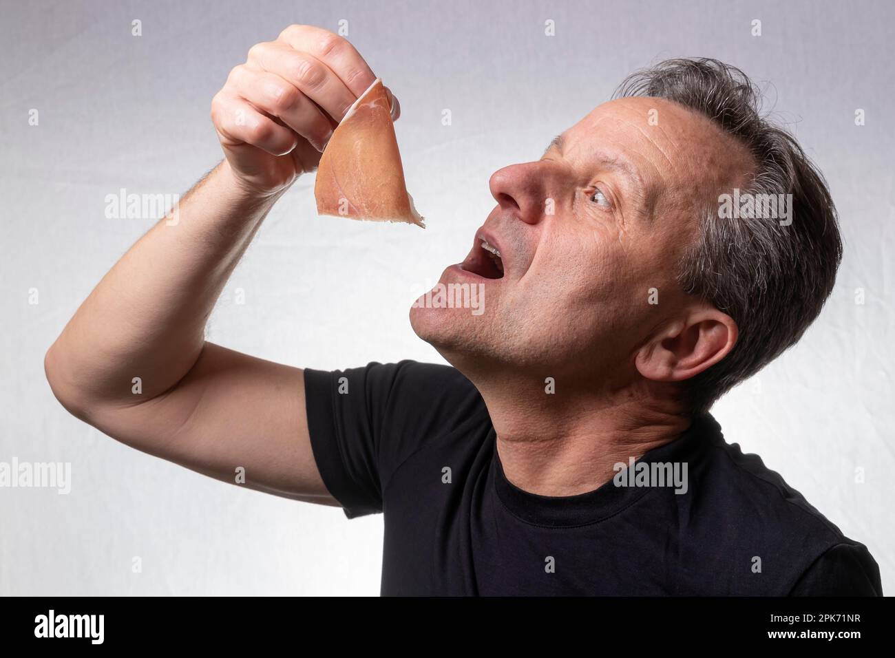 Der weiße Mann ist dabei, ein köstliches Stück geräucherten Schinken zu verschlingen Stockfoto