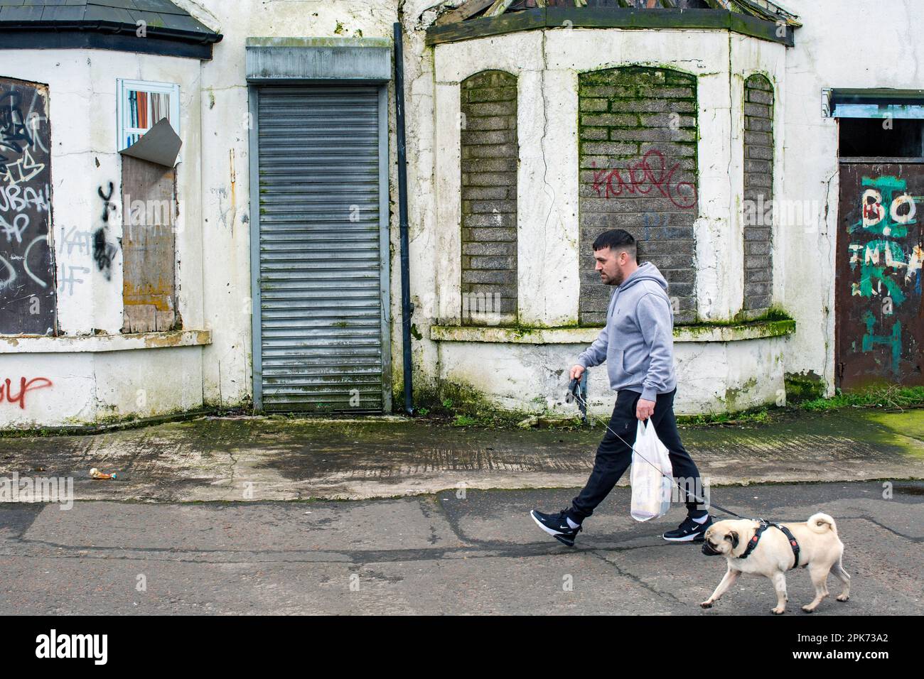 Straßenszene ein Mann geht an versteinerten Fenstern in West Belfast, Nordirland vorbei . Stockfoto