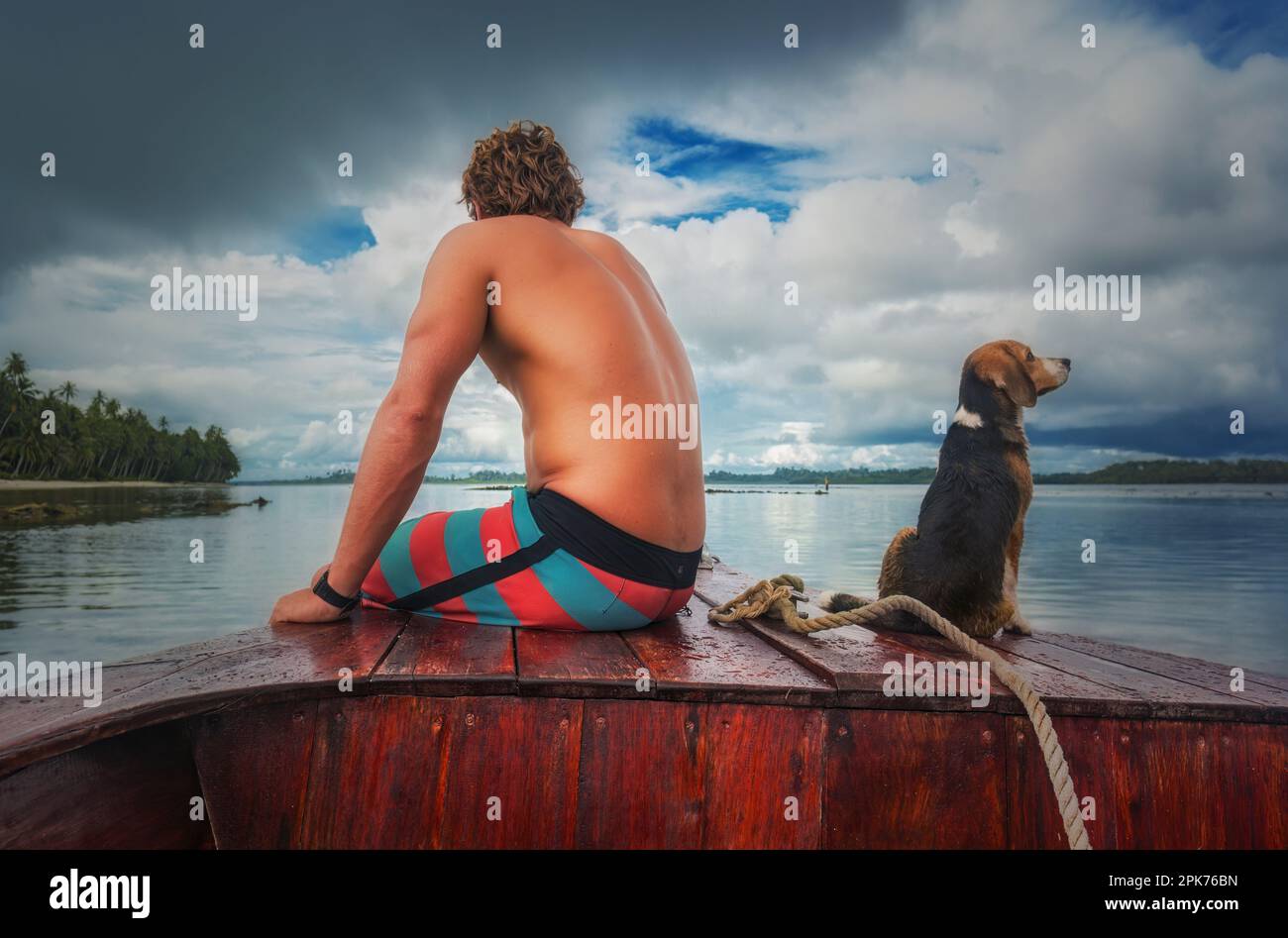 Mann und Hund blicken auf das Meer vom Bug eines kleinen hölzernen Boots aus Stockfoto