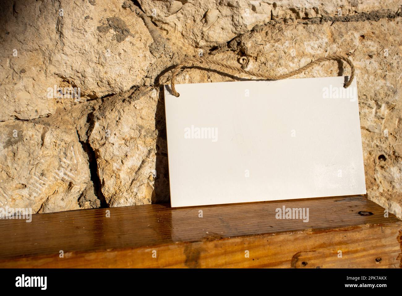 Alte Steinwand und poliertes Holz mit weißem hängendem Bildschild mit leerem freien Platz für Vorlage oder leerem Kopierbereich Stockfoto