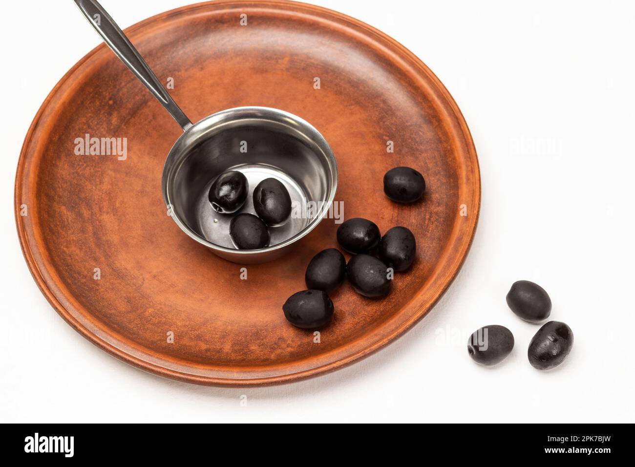 Schwarze Oliven in einer Metallschüssel und auf einer Keramikplatte. Weißer Hintergrund. Stockfoto