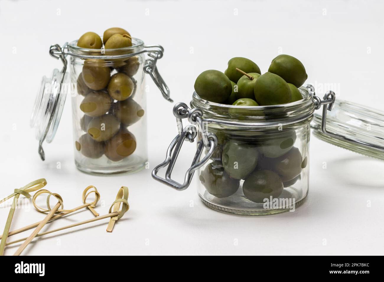 Oliven in Glasgefäßen. Spieße auf dem Tisch. Weißer Hintergrund. Stockfoto