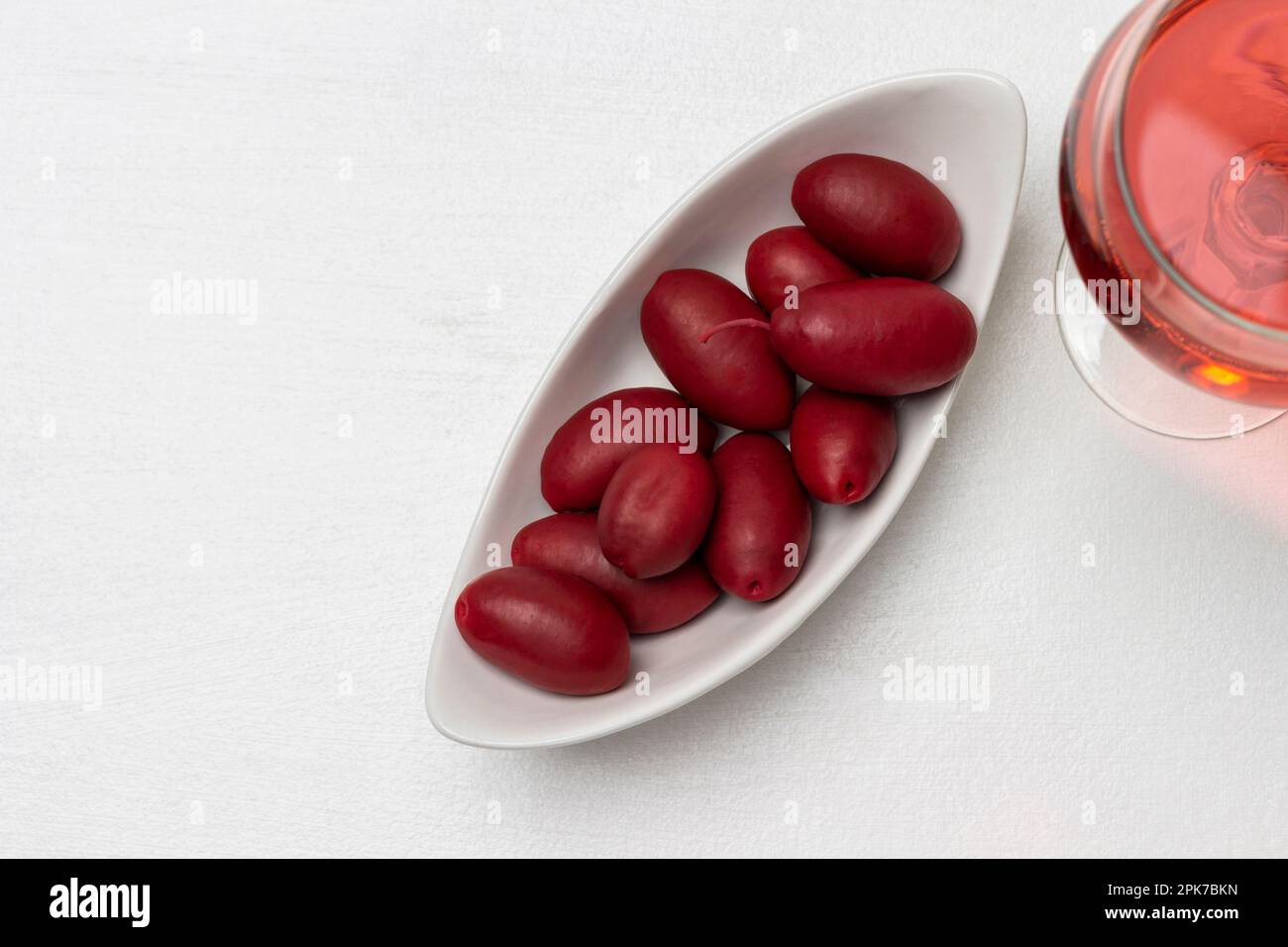 Burgunder Oliven in einer weißen Schüssel. Glas mit Rotwein. Speicherplatz kopieren. Flach verlegt. Weißer Hintergrund. Stockfoto