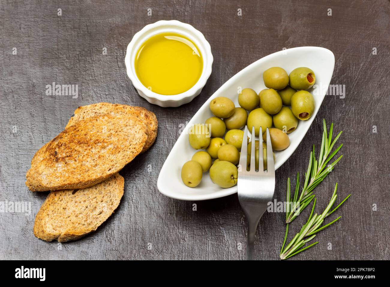 Croutons und Olivenöl in einer Schüssel. Grüne Oliven in einer weißen Schüssel. Flach verlegt. Brauner Hintergrund. Stockfoto