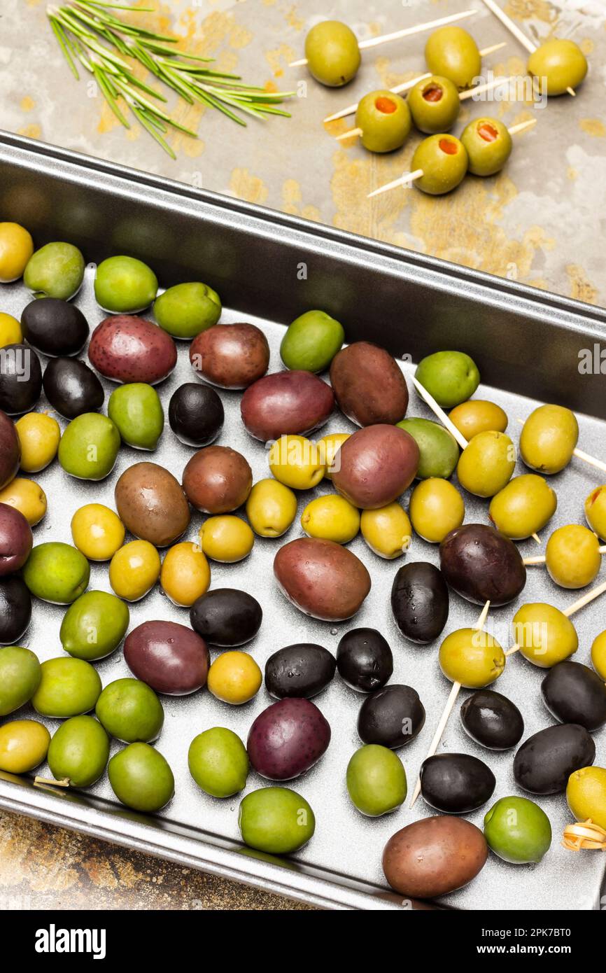 Mehrfarbige Oliven auf einem Backblech aus Metall. Flach verlegt. Rostiger Hintergrund. Stockfoto