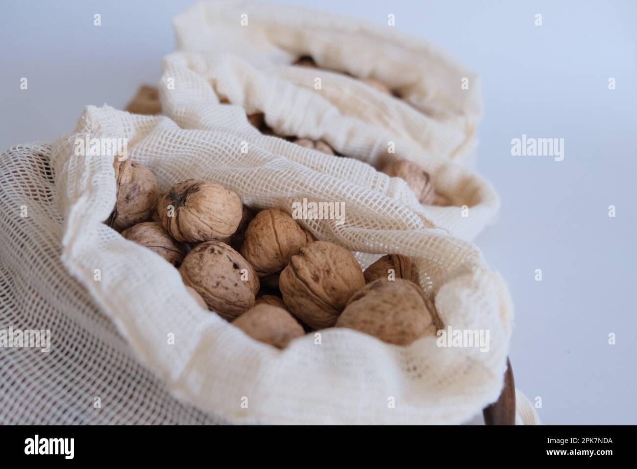 Walnüsse ohne Schale, ein Haufen Walnüsse mit Schale in drei weißen Stoffbeuteln auf weißem Hintergrund, einer nach dem anderen. Stoffbeutel voller geschälter Walnüsse. Stockfoto