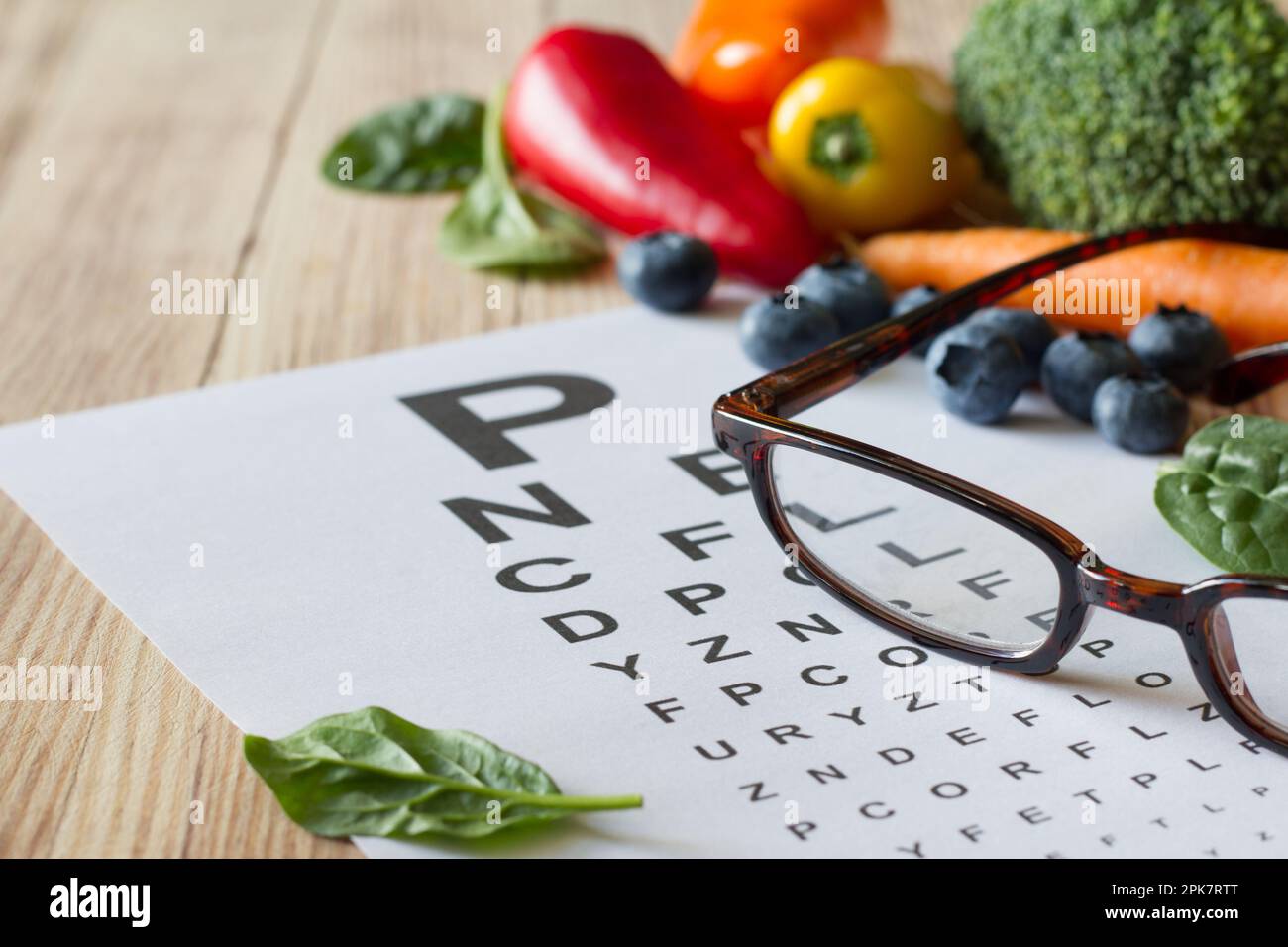 Lebensmittel für die Gesundheit der Augen, buntes Gemüse und Obst, reich an Lutein, Brille und Augentesttabelle auf Holzhintergrund, Konzept Stockfoto