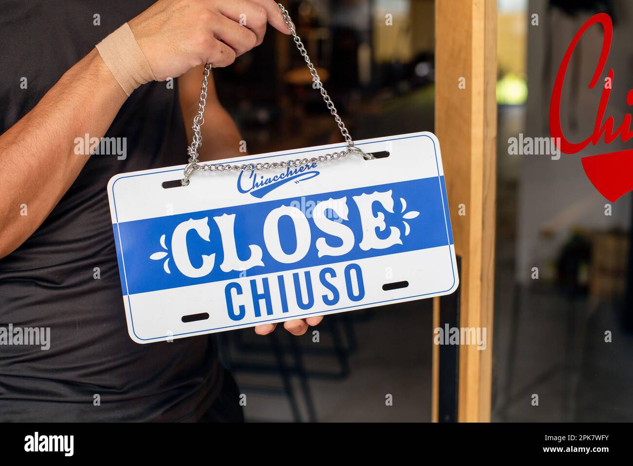 Eine Person, die ein Schild an einer Restauranttür aufhängt und "Schließen" liest. Geschlossen, zwei Sprachen, Englisch und Italienisch. Stockfoto