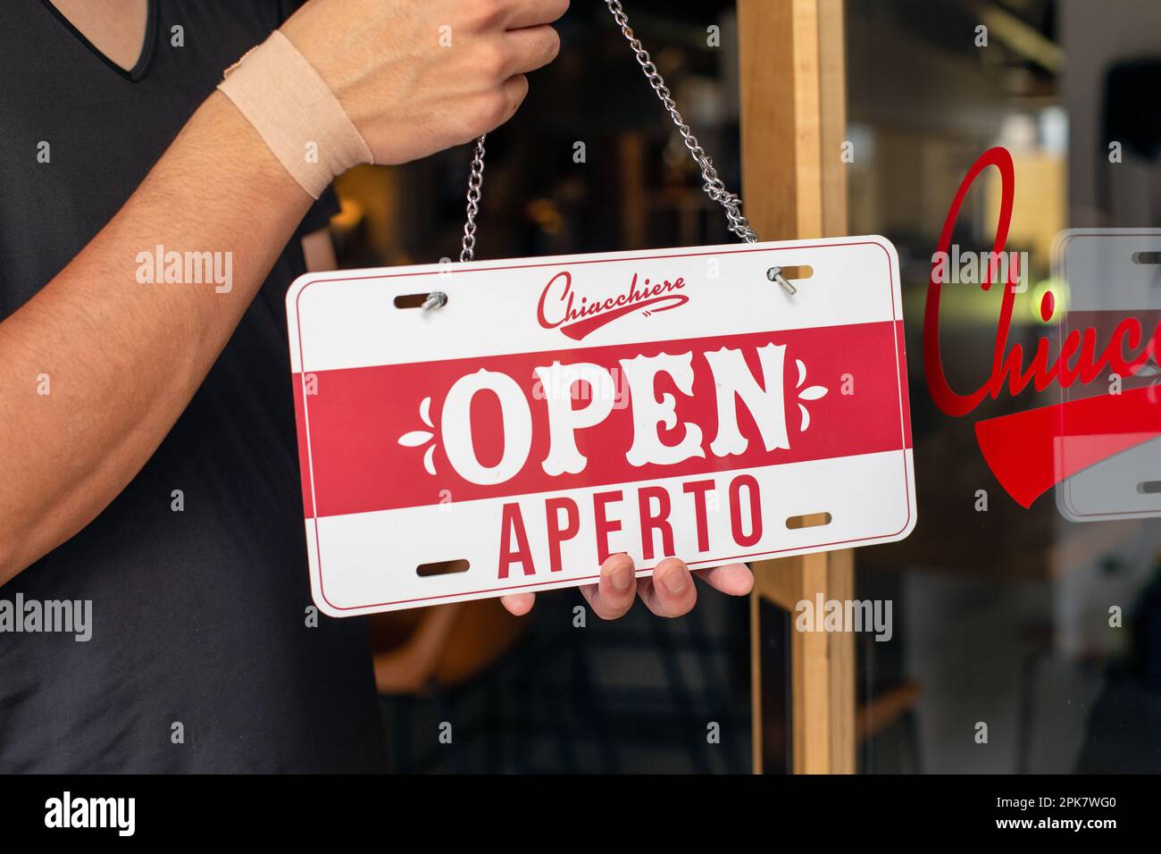 Ein Mann hängt ein Open-Schild an einer Restauranttür auf. Zwei Sprachen, Italienisch und Englisch. Stockfoto