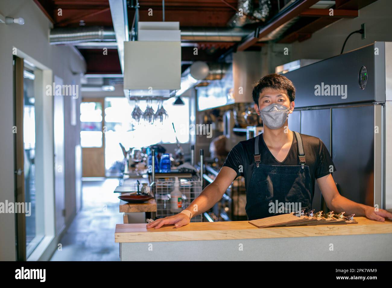 Ein Mann mit einer Gesichtsmaske an der Theke einer Restaurantküche, der Besitzer oder Manager. Stockfoto