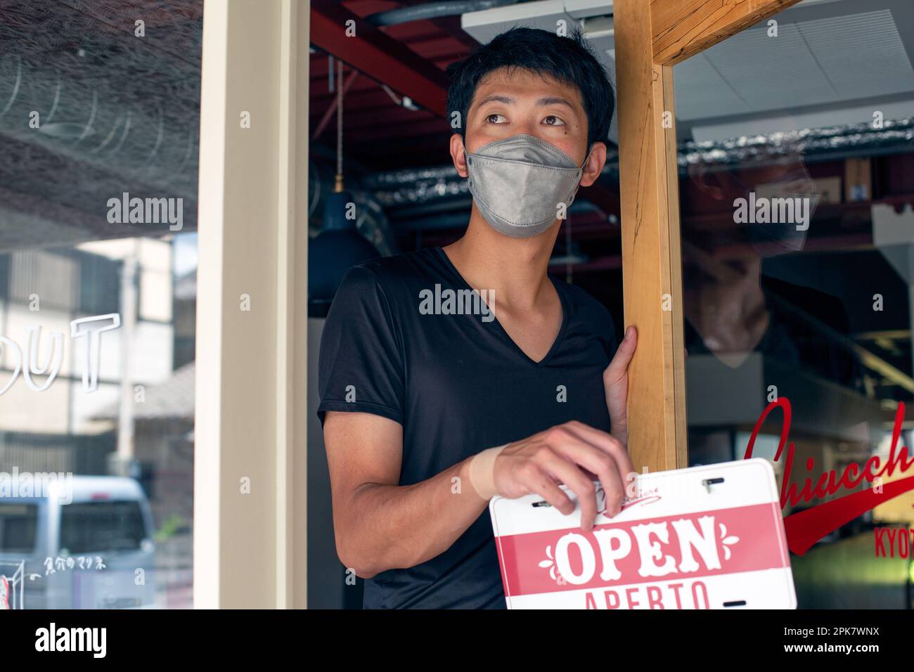 Ein Mann mit einer Gesichtsmaske hängt ein Open-Schild an einer Tür des italienischen Restaurants auf. Zwei Sprachen, Italienisch und Englisch. Stockfoto