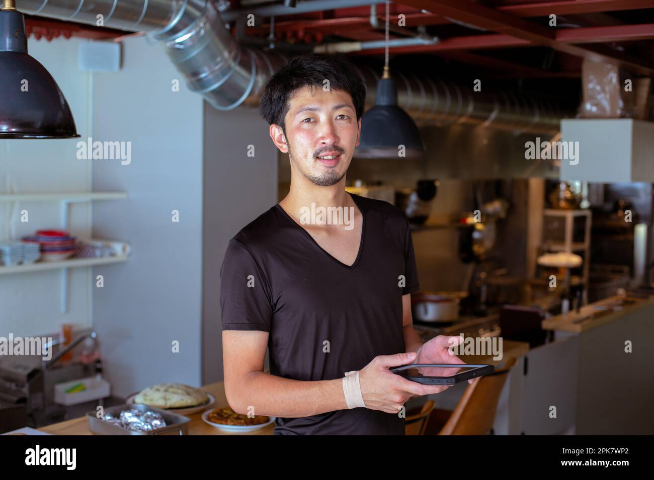 Ein Mann, der in einem Restaurant bei einer offenen Küche arbeitet und ein digitales Tablet in der Hand hält. Stockfoto