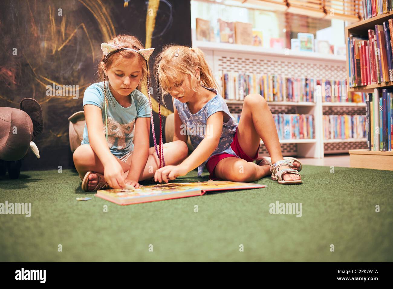 Zwei Grundschulmädchen lösen Rätsel und rätsel in der Schulbibliothek. Schüler lernen aus Büchern. Schüler, die Spaß in der Bibliothek haben. Zurück in die Schule Stockfoto