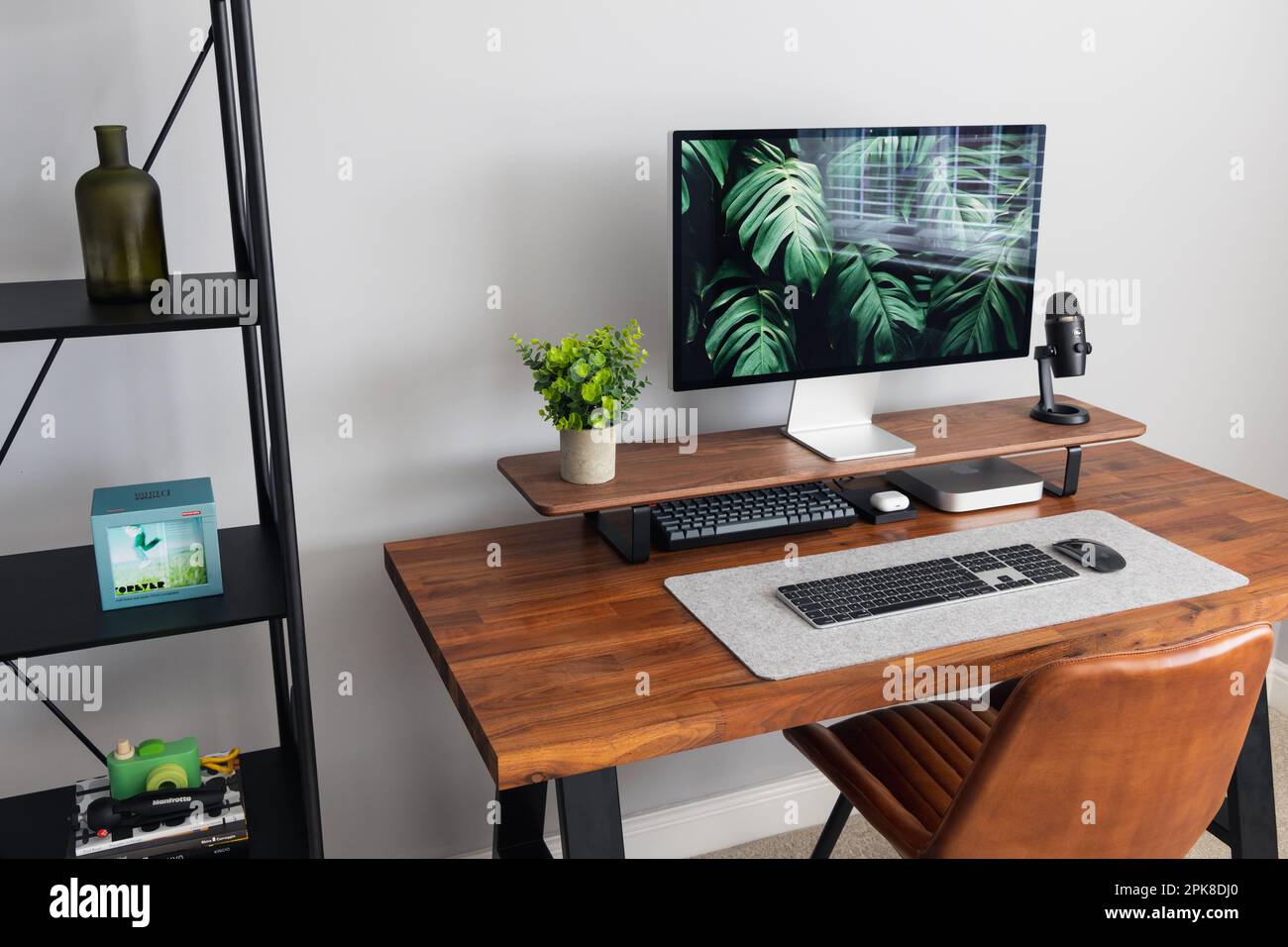 LONDON - 06. APRIL 2023: Minimaler Schreibtischaufbau in einem modernen Heimbüro mit Apple-Computertastatur, Schreibtisch aus Walnussholz und Pflanzen Stockfoto