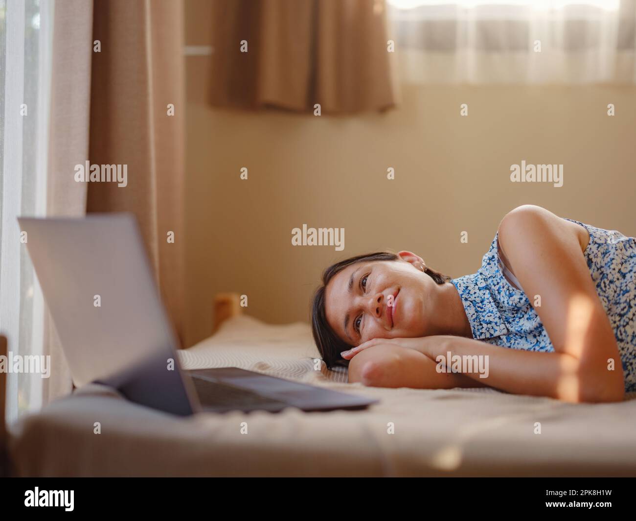 Glückliche junge asiatische Frau mit Laptop im Schlafzimmer in einem winzigen Haus, Wochenendausflug und Remote Office Idee. Winzige Häuser und kleines Wohnkonzept. Stockfoto